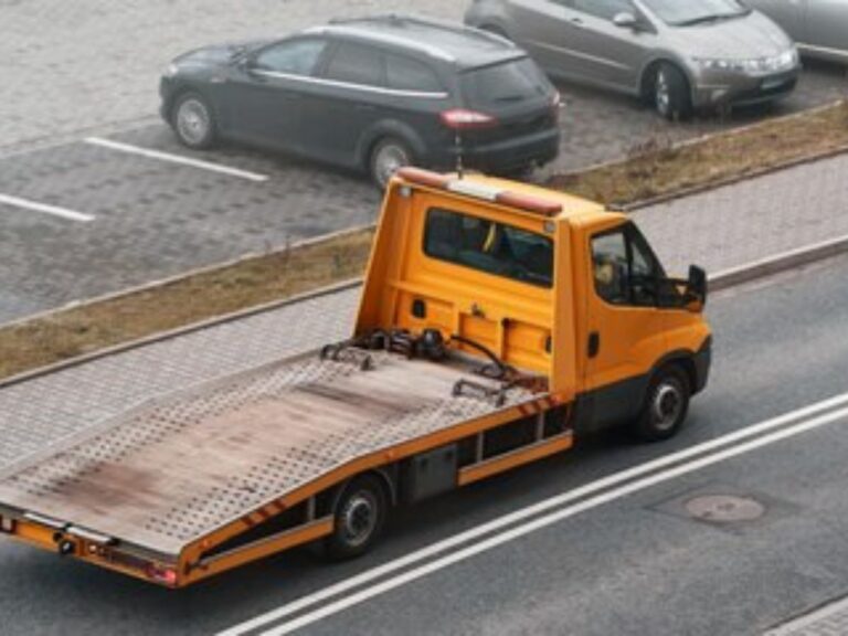 Flatbed tow truck loading a car on Point Cook Road with shopping centre in background